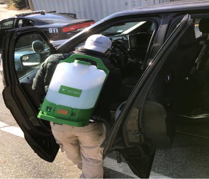 technician with a back pack spray disinfecting a police car