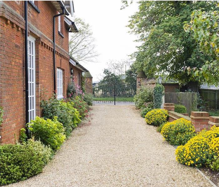 a gated long brown pebble driveway tucked next to a large brick home